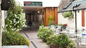 An outdoor seating area with tables and chairs, a sign for Milan Restaurant, and various potted plants. - Black Bull Inn (Wooler)