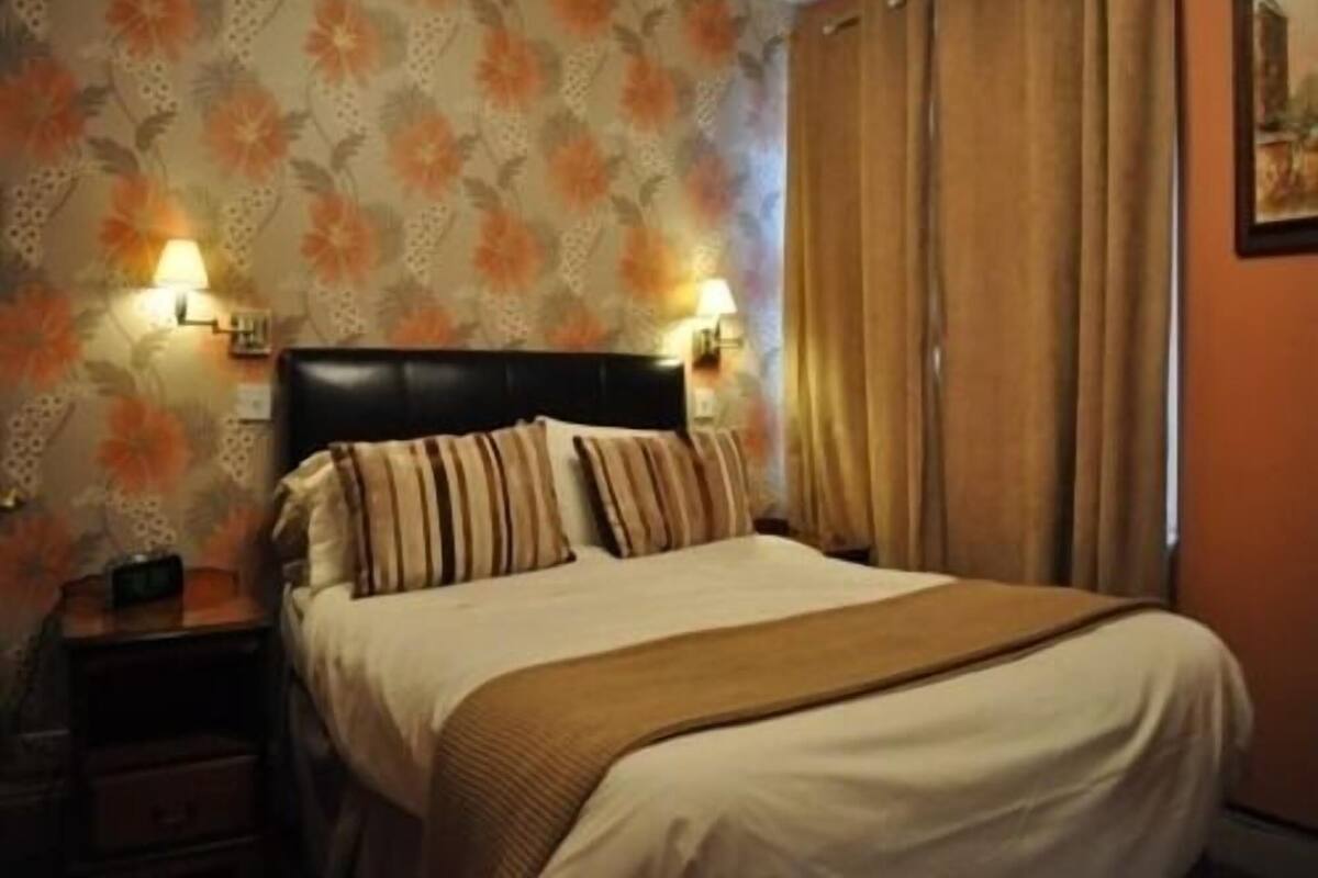 A hotel room with a bed, nightstands, a lamp, and a curtain.