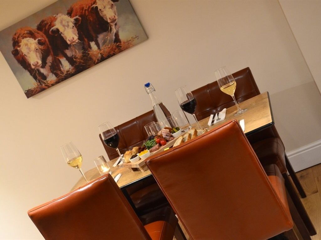 A dining area with a table set for four, featuring a bottle of water, wine glasses, and a meal.
