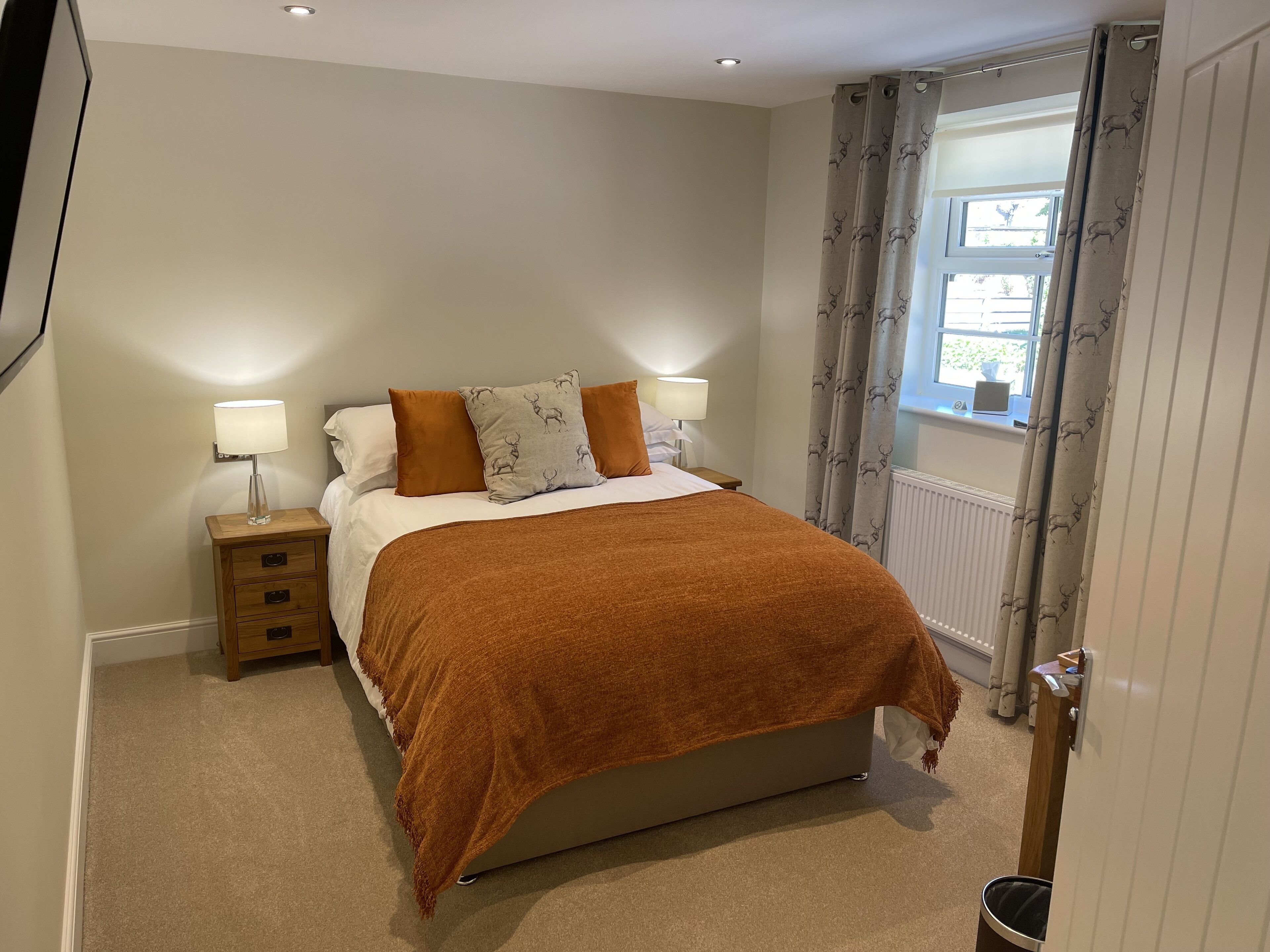 A bedroom with a bed, two bedside tables, a nightstand, a window with curtains, and a radiator.