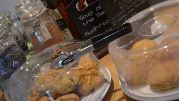 A table with jars of condiments, a sign for soup of the day, and two containers of food items.
