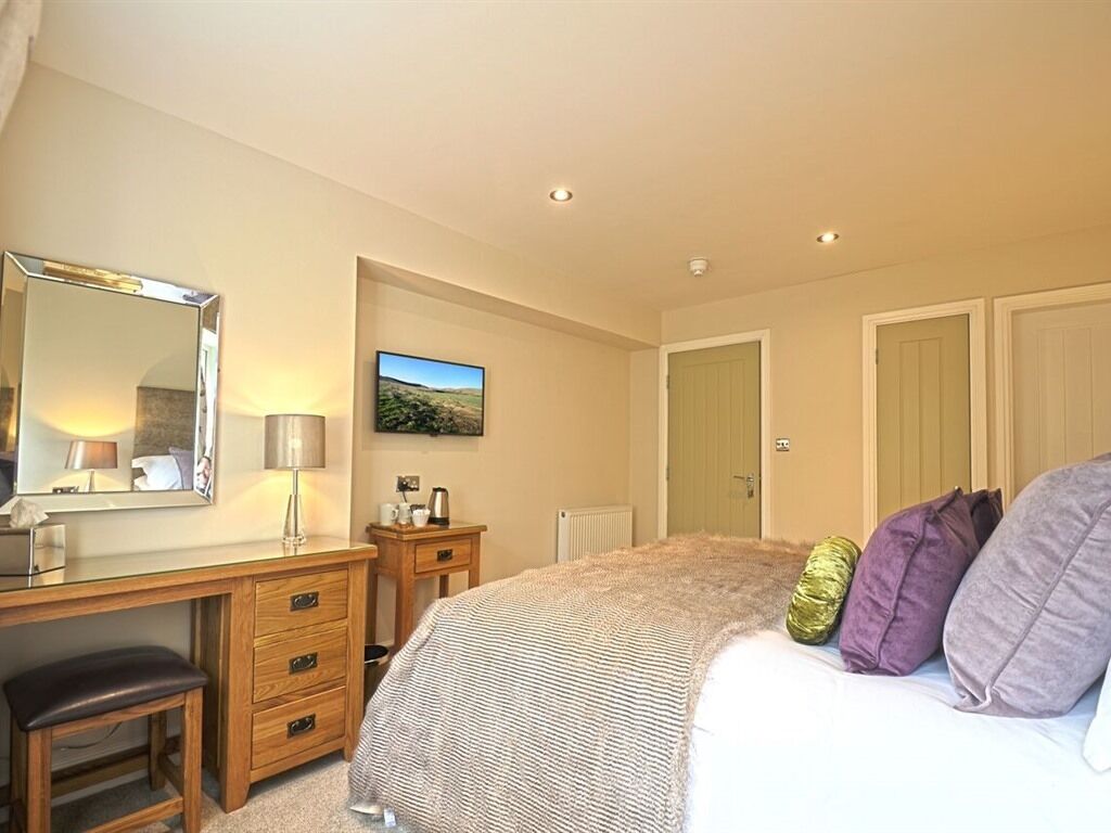 A bedroom with a bed, a dresser, a mirror, a lamp, a painting, and a door.