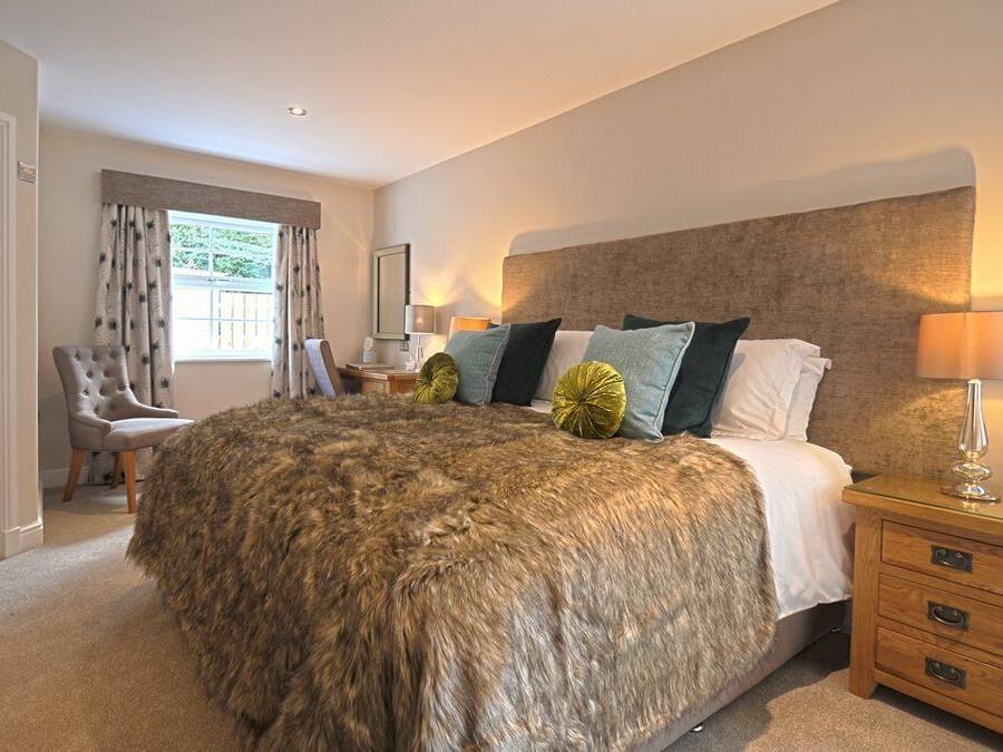 A bedroom with a large bed, a chair, a nightstand, and a window with curtains.