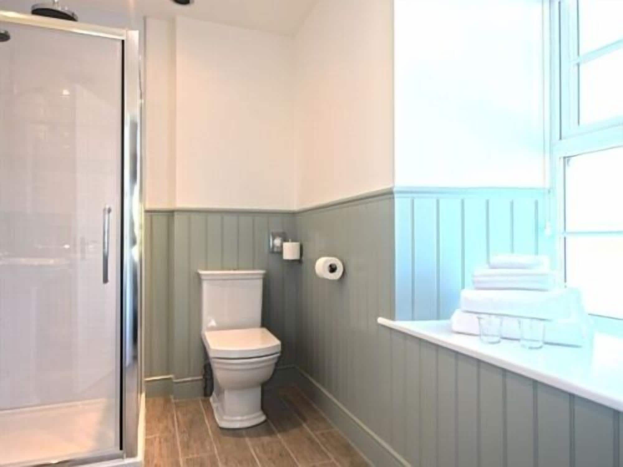 Un baño con inodoro, dispensador de toallas de papel y ventana con perchero.