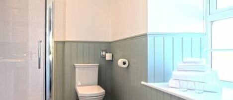Un baño con inodoro, dispensador de toallas de papel y ventana con perchero.