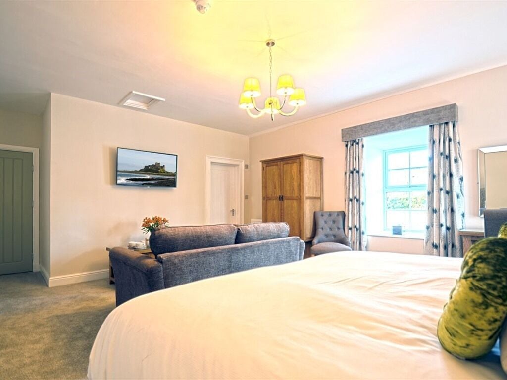 A bedroom with a large bed, a chair, a wooden wardrobe, a painting on the wall, and a window with curtains.