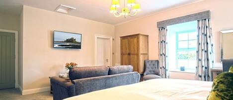 A bedroom with a large bed, a chair, a wooden wardrobe, a painting on the wall, and a window with curtains.