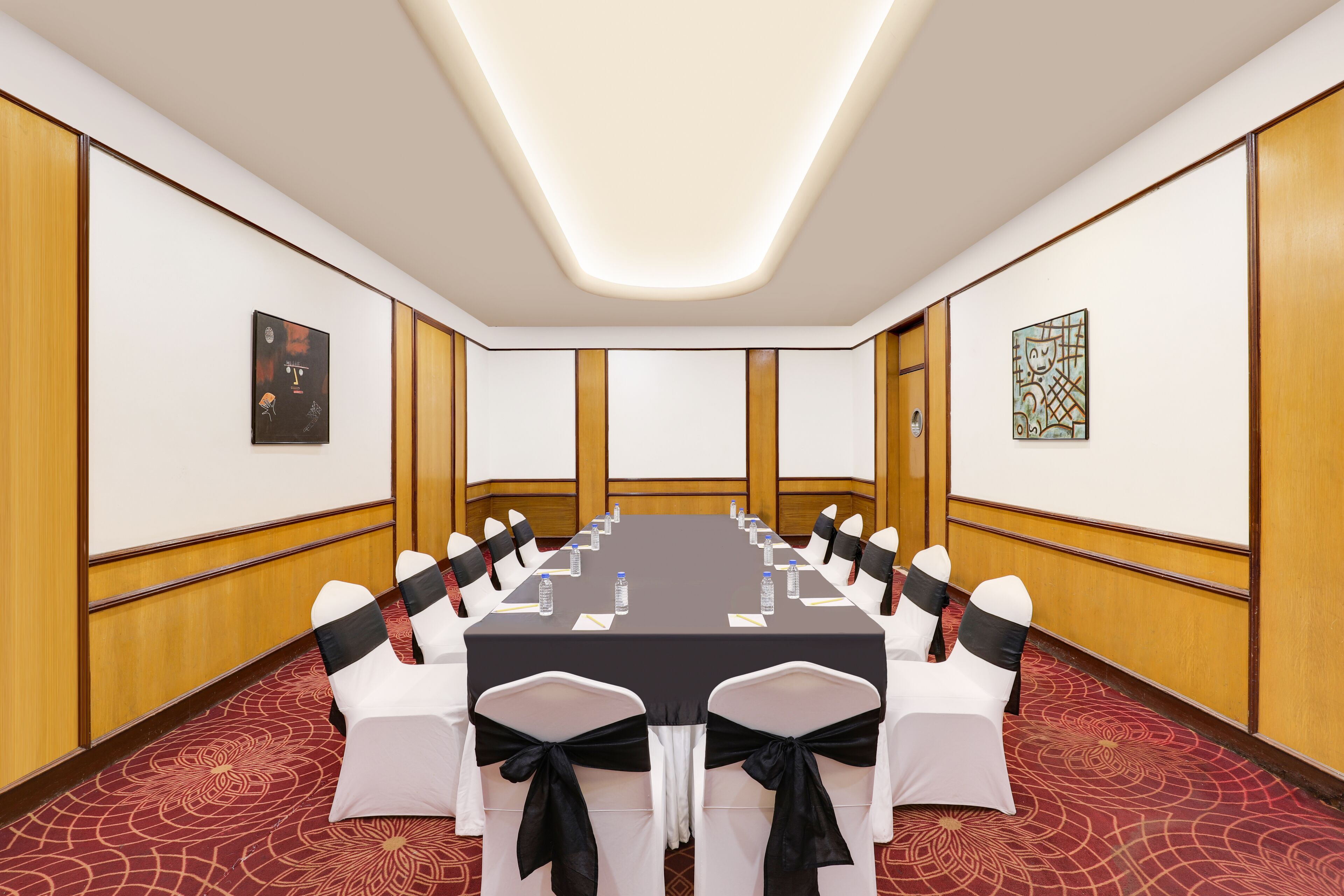 A conference room with a long table, white chairs with black sashes, and framed artwork on the walls.