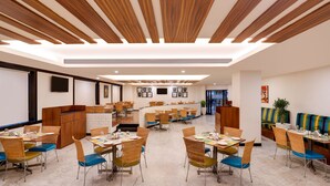 A spacious dining area with multiple tables and chairs, a kitchen area, and a seating area with a colorful sofa. - Lemon Tree Hotel, Indore (Indore)