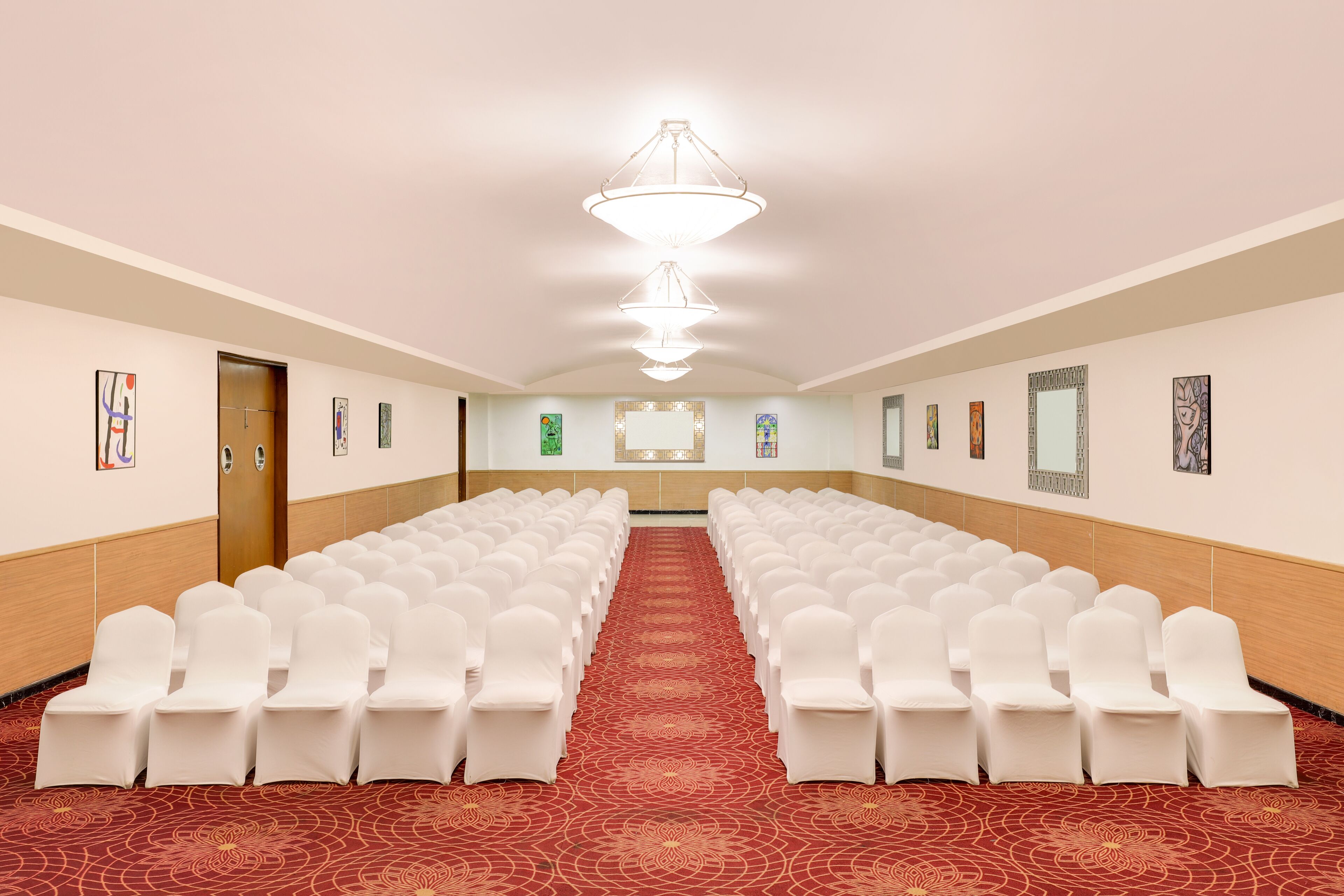 Un salón de conferencias con filas de sillas blancas, una alfombra roja y una araña.