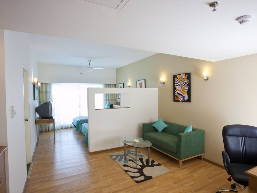 A modern living room with a green sofa, a black office chair, a glass coffee table, and a wooden floor.