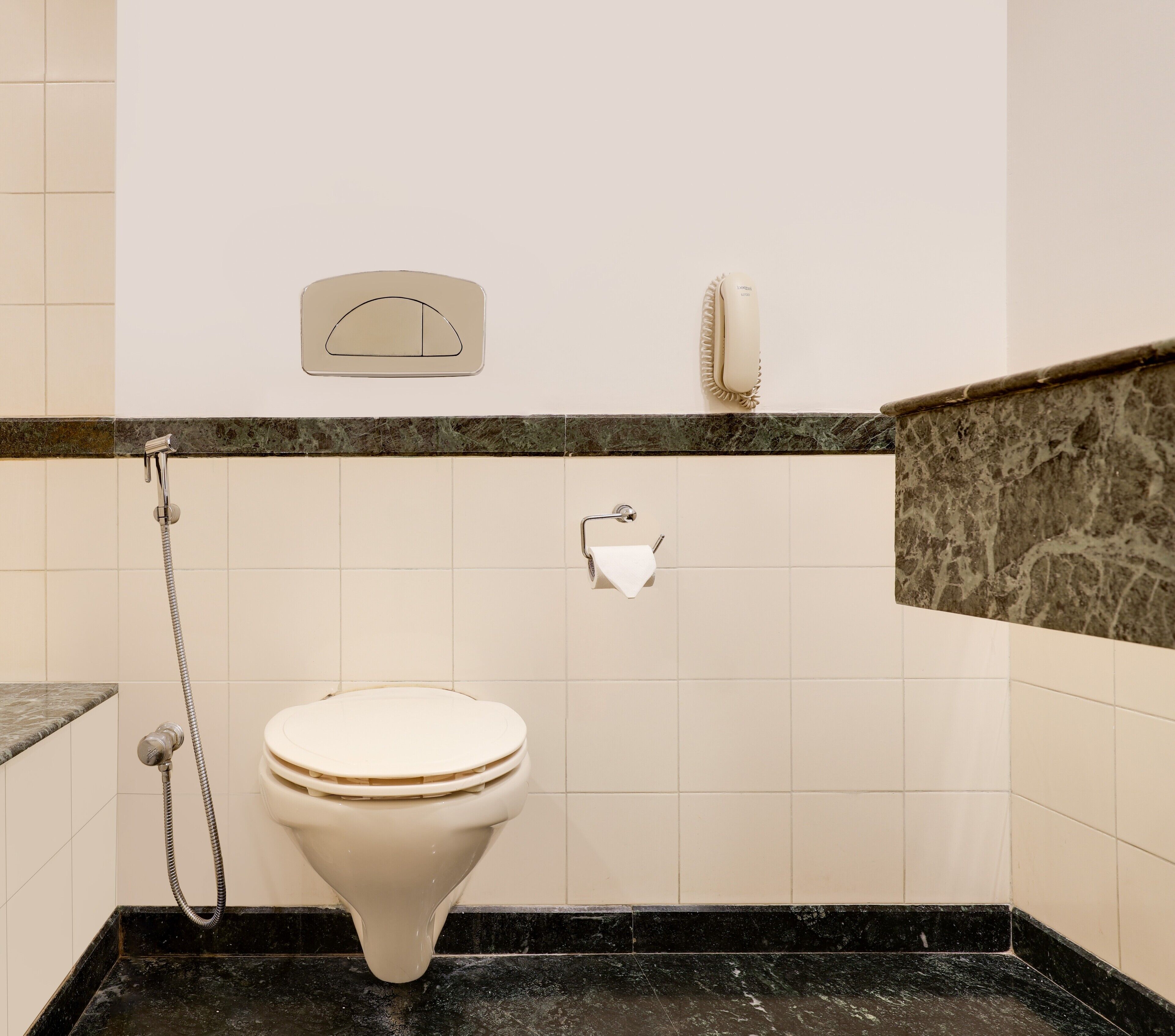A bathroom with a toilet, a shower, a towel dispenser, and a telephone.