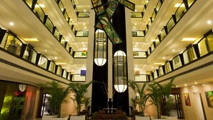 A multi-level hotel lobby with a central decorative sculpture, multiple floors with balconies, and a seating area with potted plants. - Lemon Tree Hotel, Indore (Indore)