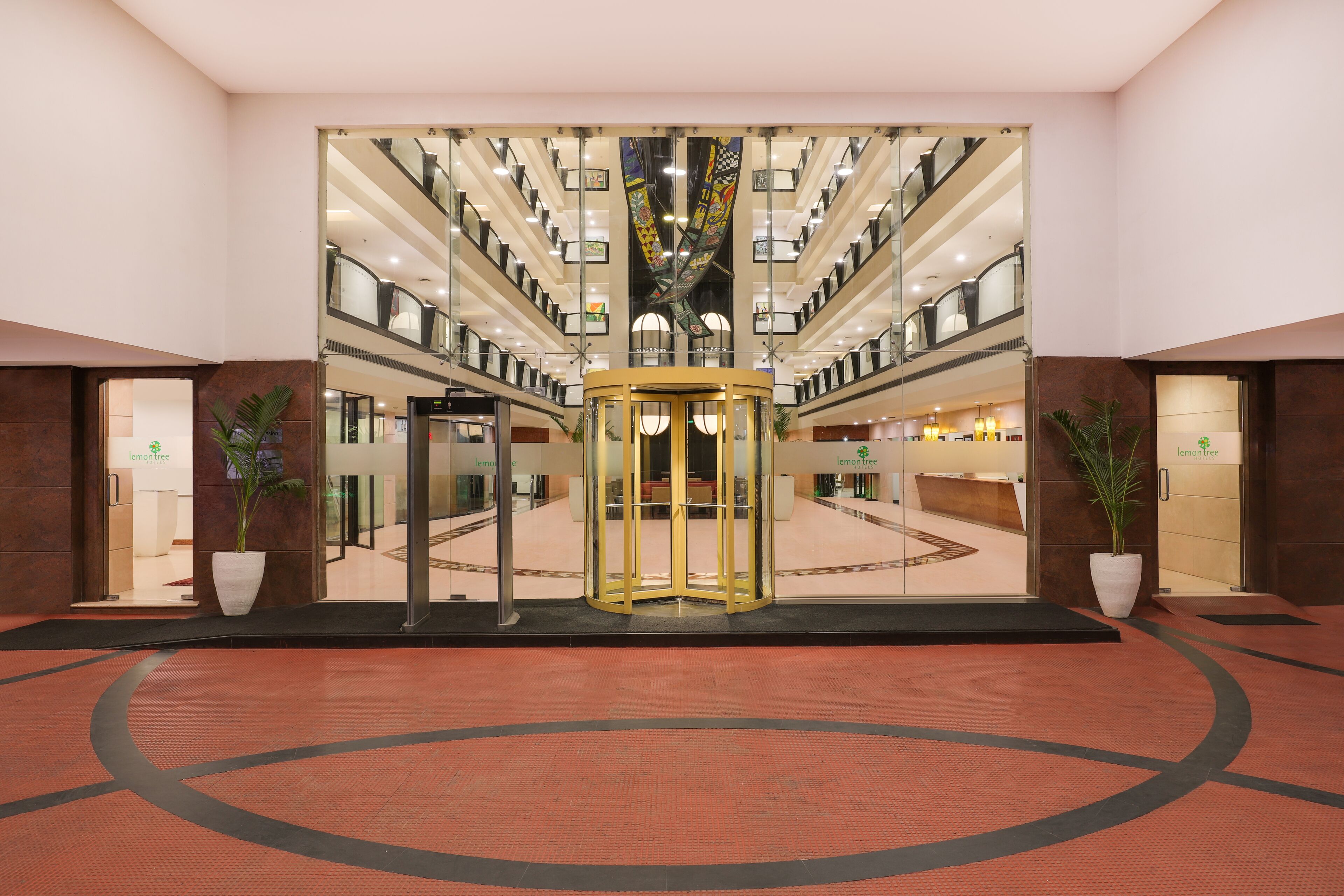 En hotellobby med en roterande dörr, krukväxter och en central, cirkelformad design i golvet.
