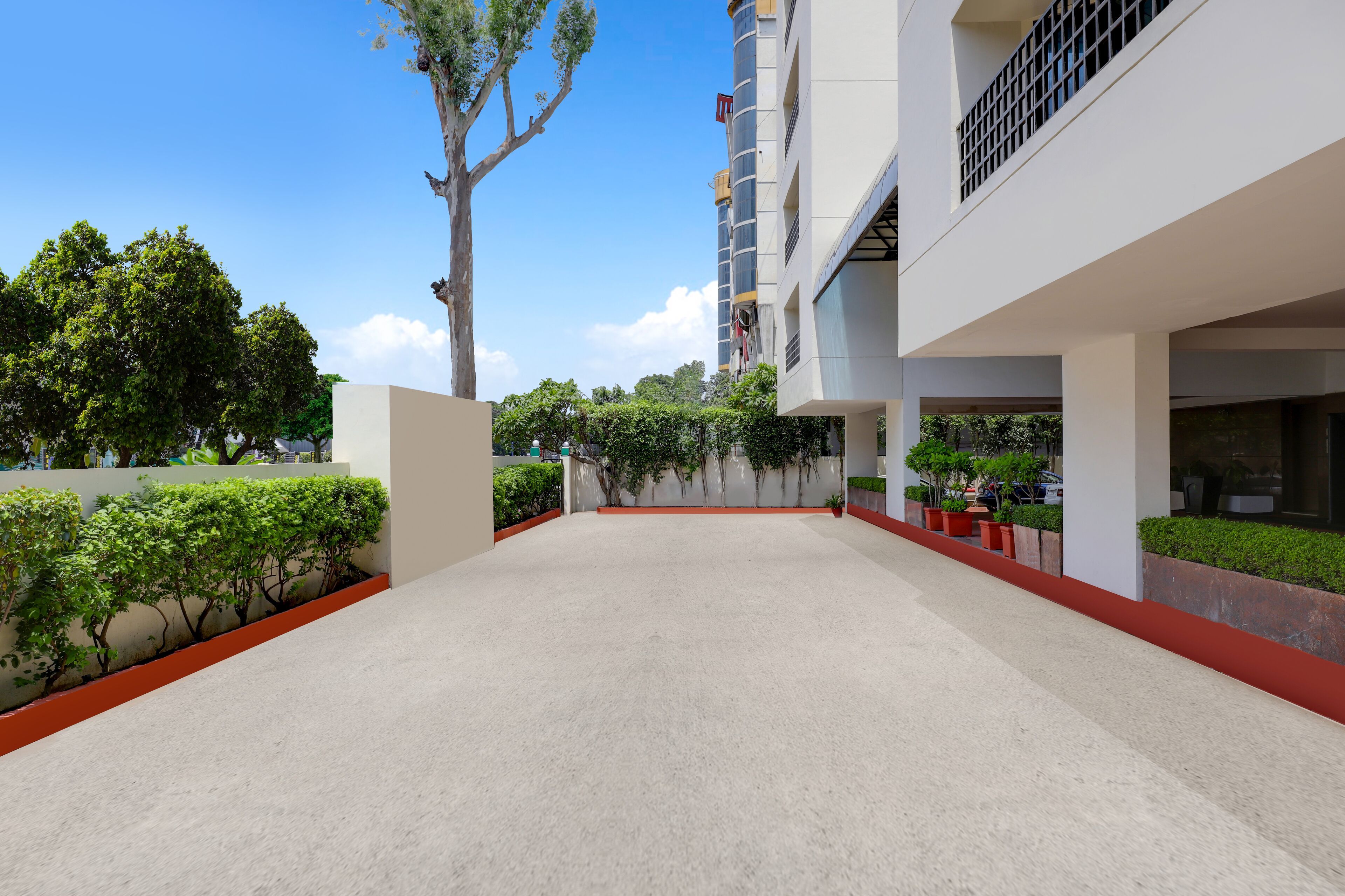 Un edificio moderno con patio, que presenta fachada blanca, detalles rojos y jardines verdes.