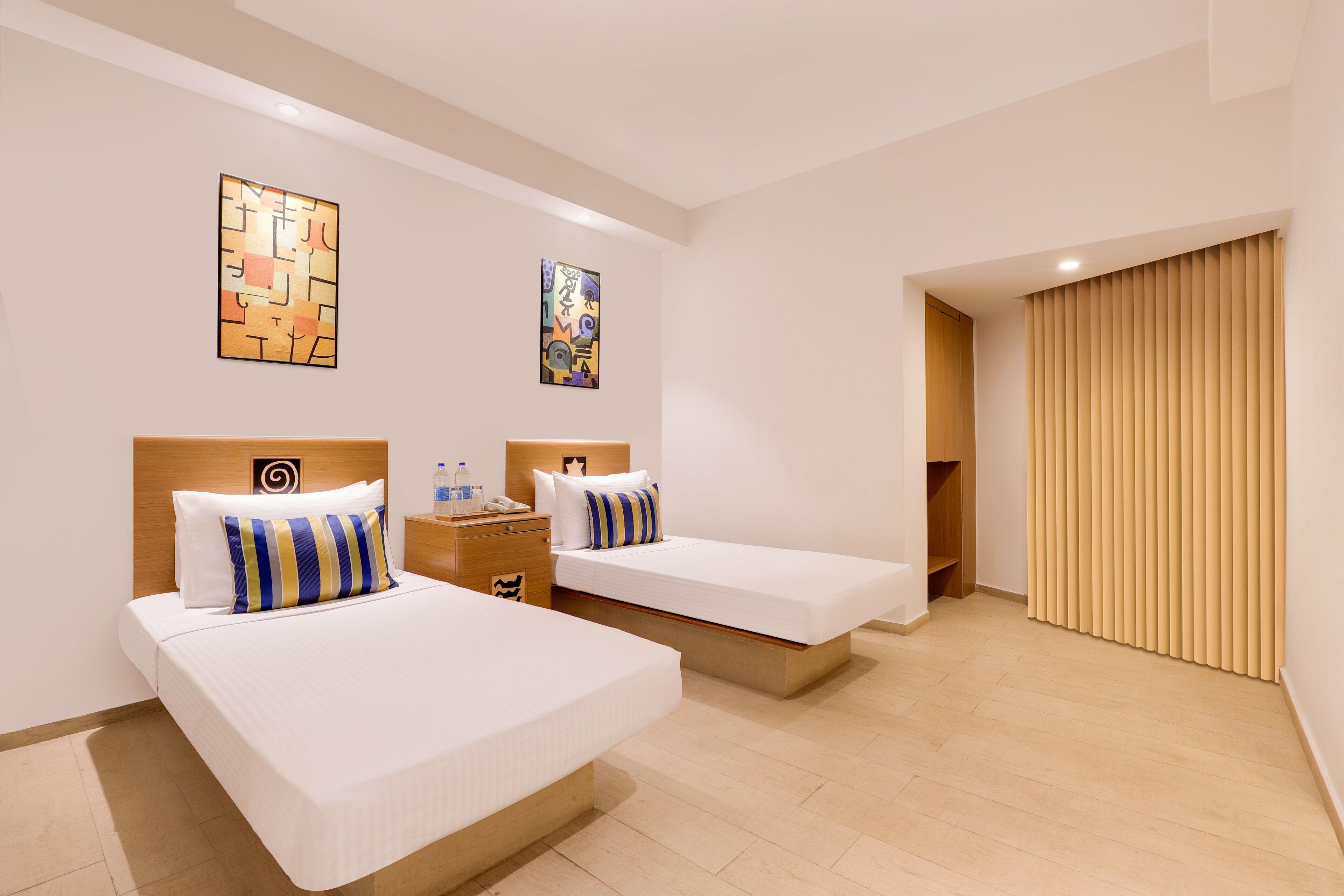 A hotel room with two single beds, a wooden headboard, a nightstand, and a window with blinds.
