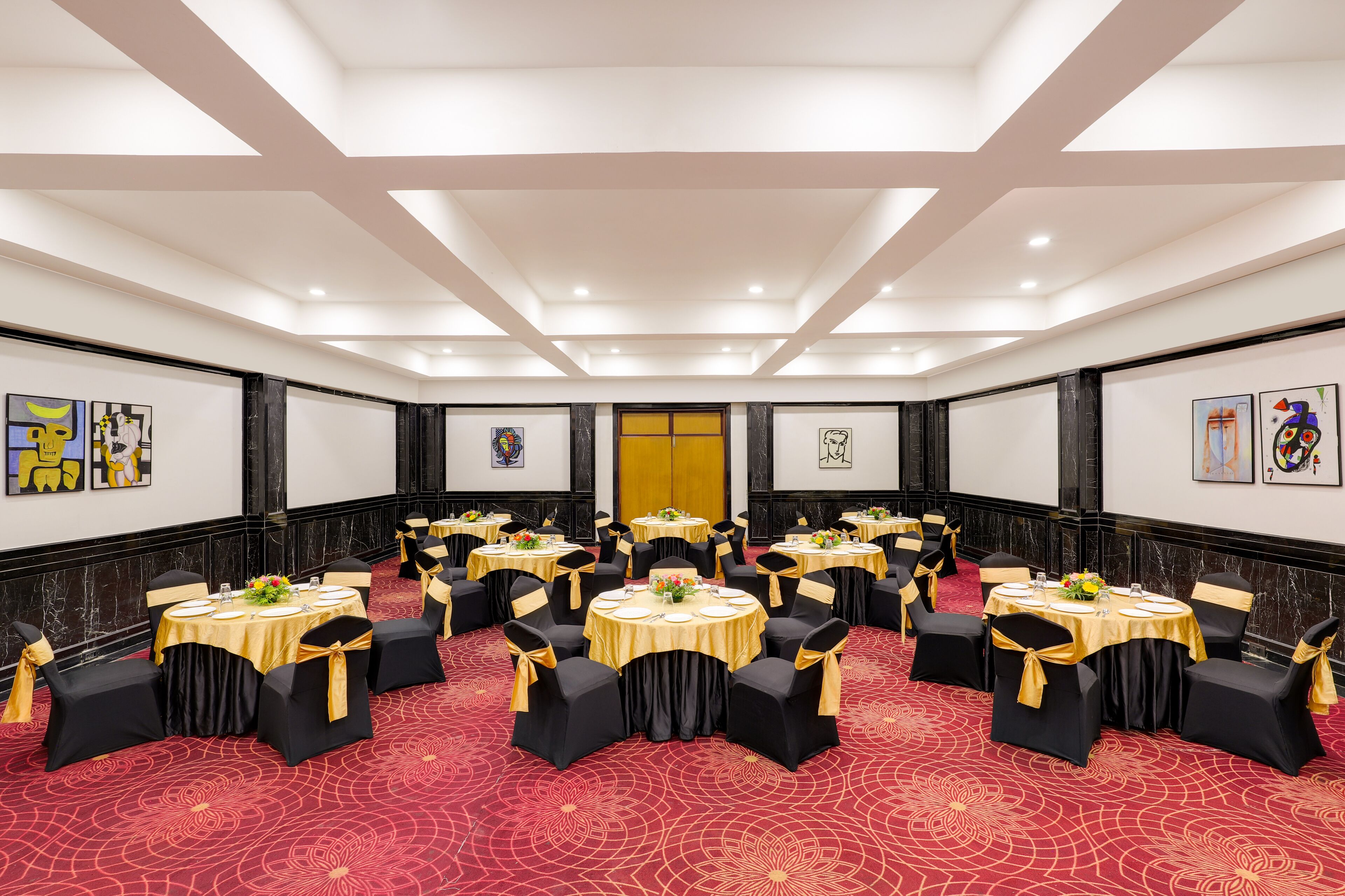 A conference room with round tables, black chairs with gold sashes, and a red patterned carpet.