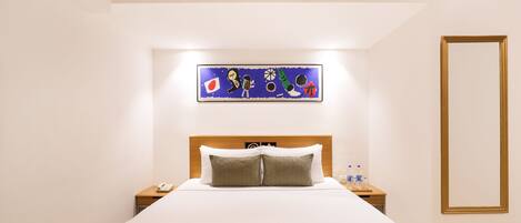 Ein Hotelzimmer mit einem großen Bett, einem Nachttisch mit Telefon, einer Nachttischlampe und Wasserflaschen sowie einem Bild an der Wand über dem Bett.