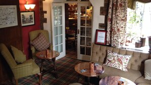 A cozy room with a sofa, chairs, and a table. There is a door leading to another room with shelves. - The Black Swan (Kirkby Stephen)
