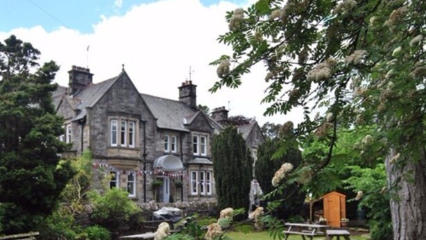 A large stone building with multiple chimneys, surrounded by a well-maintained lawn and picnic tables. - The Black Swan (Kirkby Stephen)