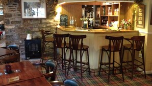A bar area with wooden stools, a bar counter, and a stone wall. - The Black Swan (Kirkby Stephen)