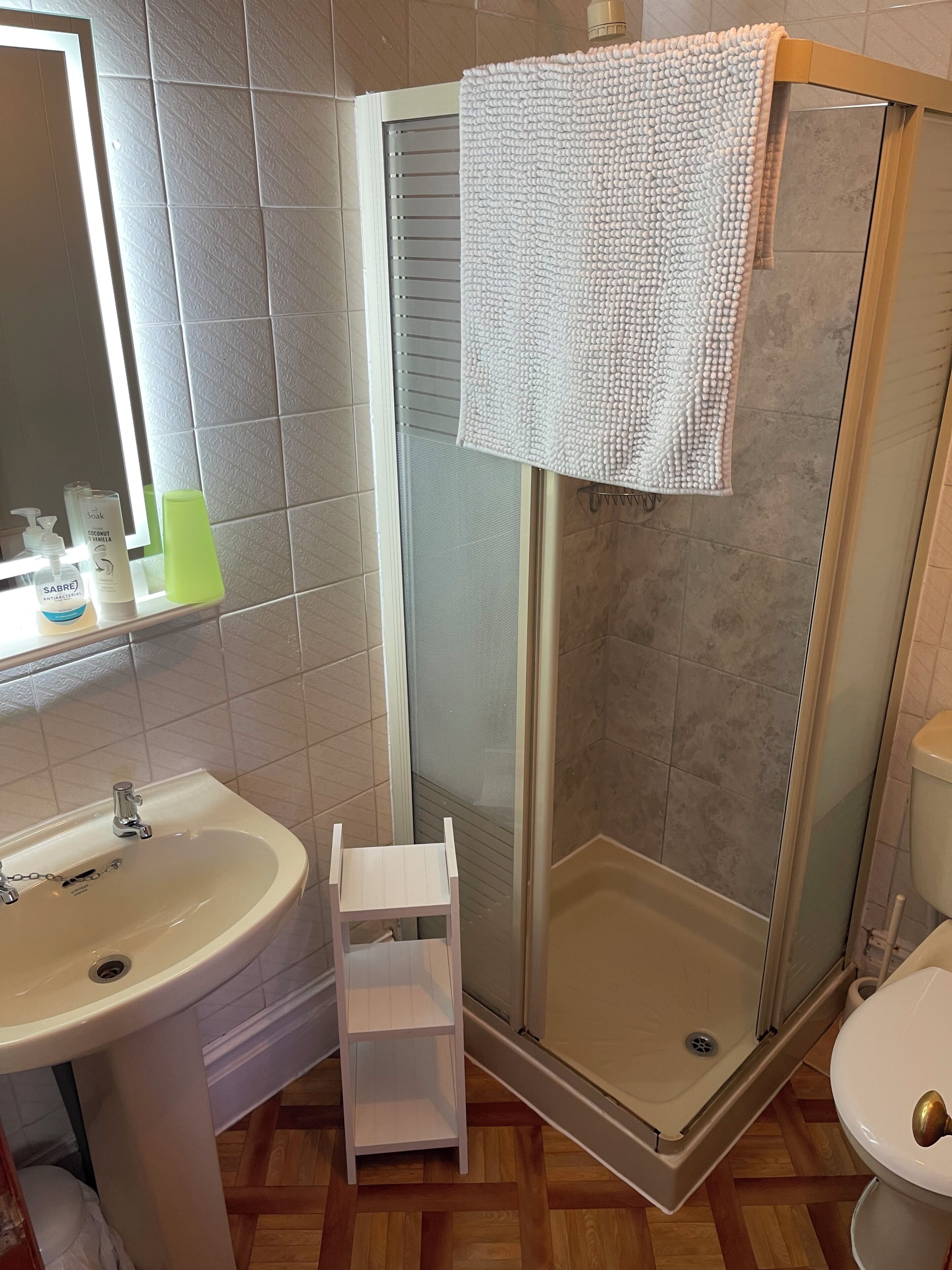 A bathroom with a shower, sink, toilet, and a shelf.