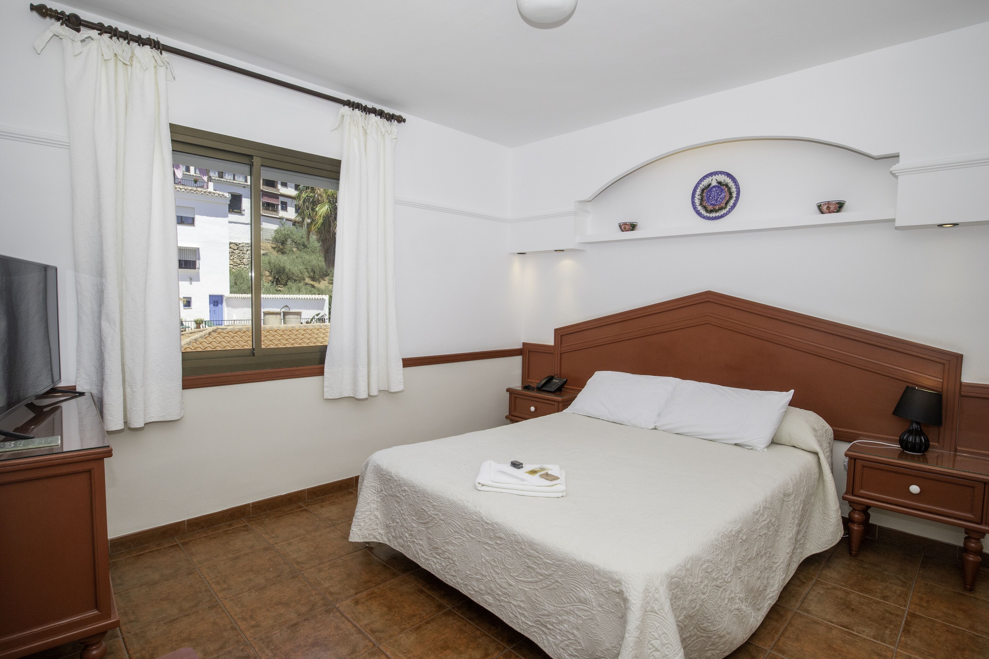 A hotel room with a bed, a nightstand, a television, and a window with curtains.