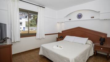 A hotel room with a bed, a nightstand, a television, and a window with curtains.