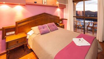A hotel room with a large bed, wooden headboard, and a balcony with chairs.