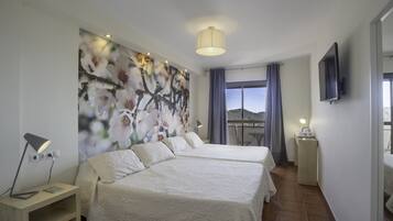 Habitación de hotel con dos camas, un cuadro grande con motivos florales en la pared, un televisor montado y un balcón con vistas.