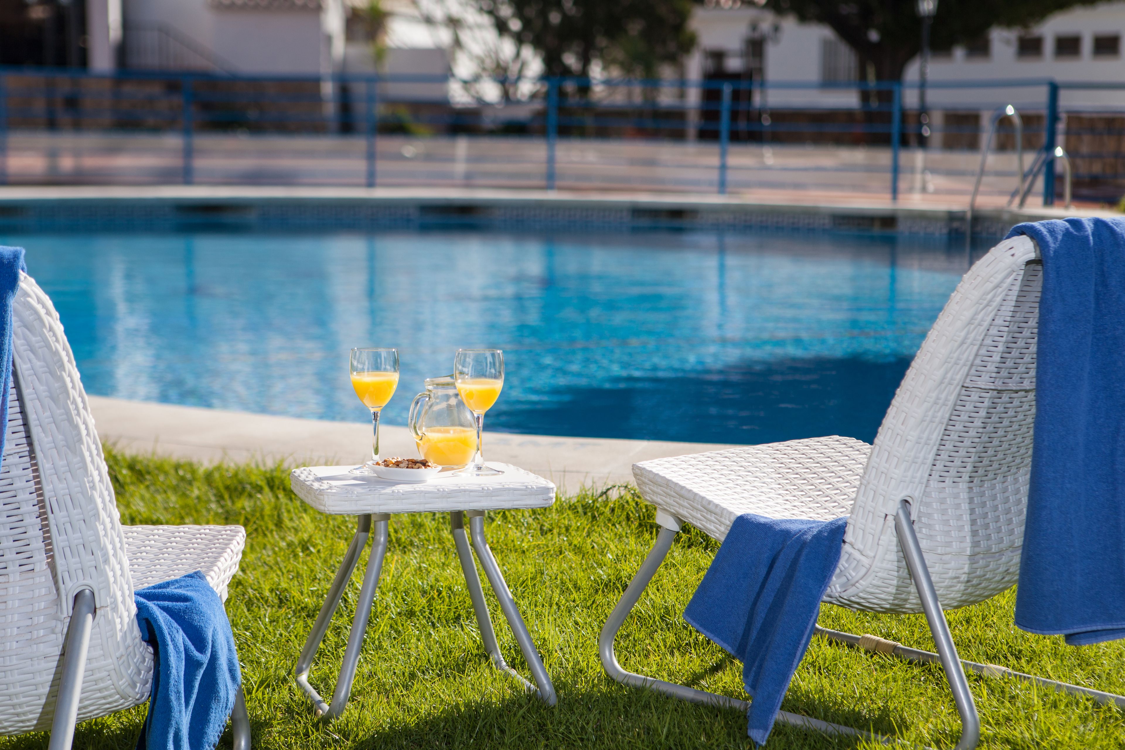 Un espacio junto a la piscina con dos sillones reclinables, una mesita con bebidas y una vista despejada de la piscina.
