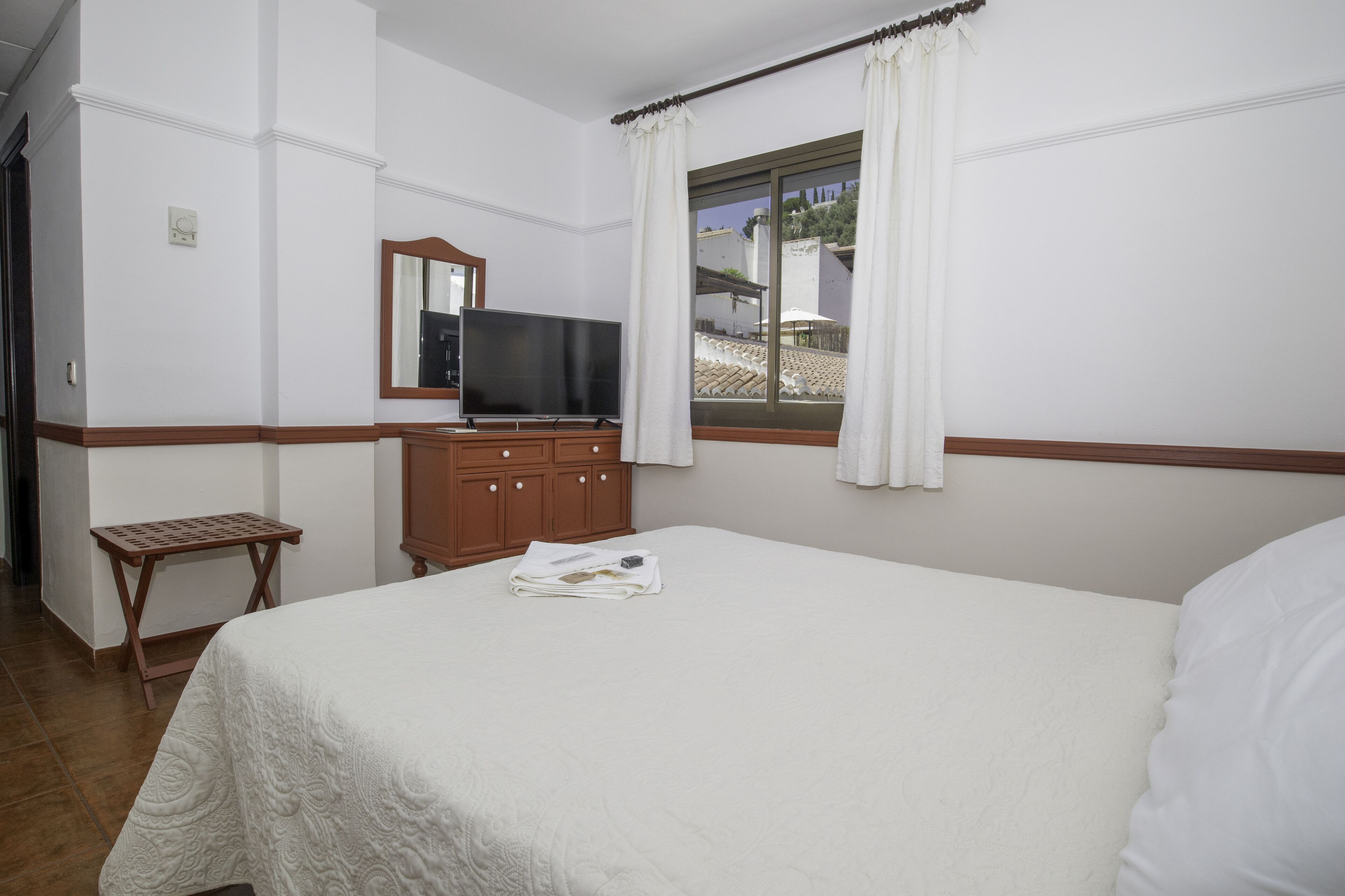 Une chambre d’hôtel avec un grand lit, une commode en bois, une télévision et une fenêtre avec des rideaux.