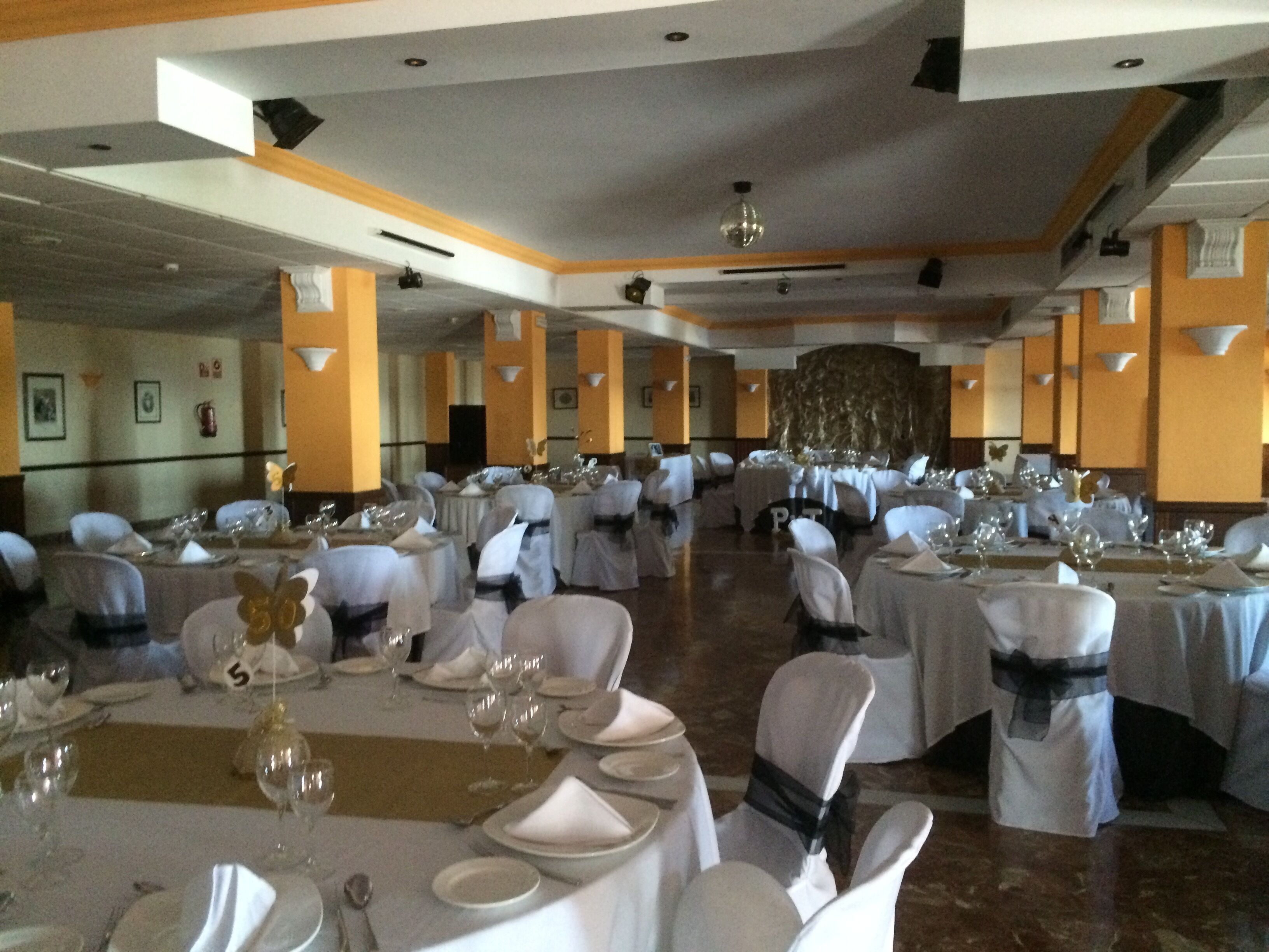 Une salle de banquet avec des tables rondes dressées pour le repas, des chaises blanches et une scène à l’avant.