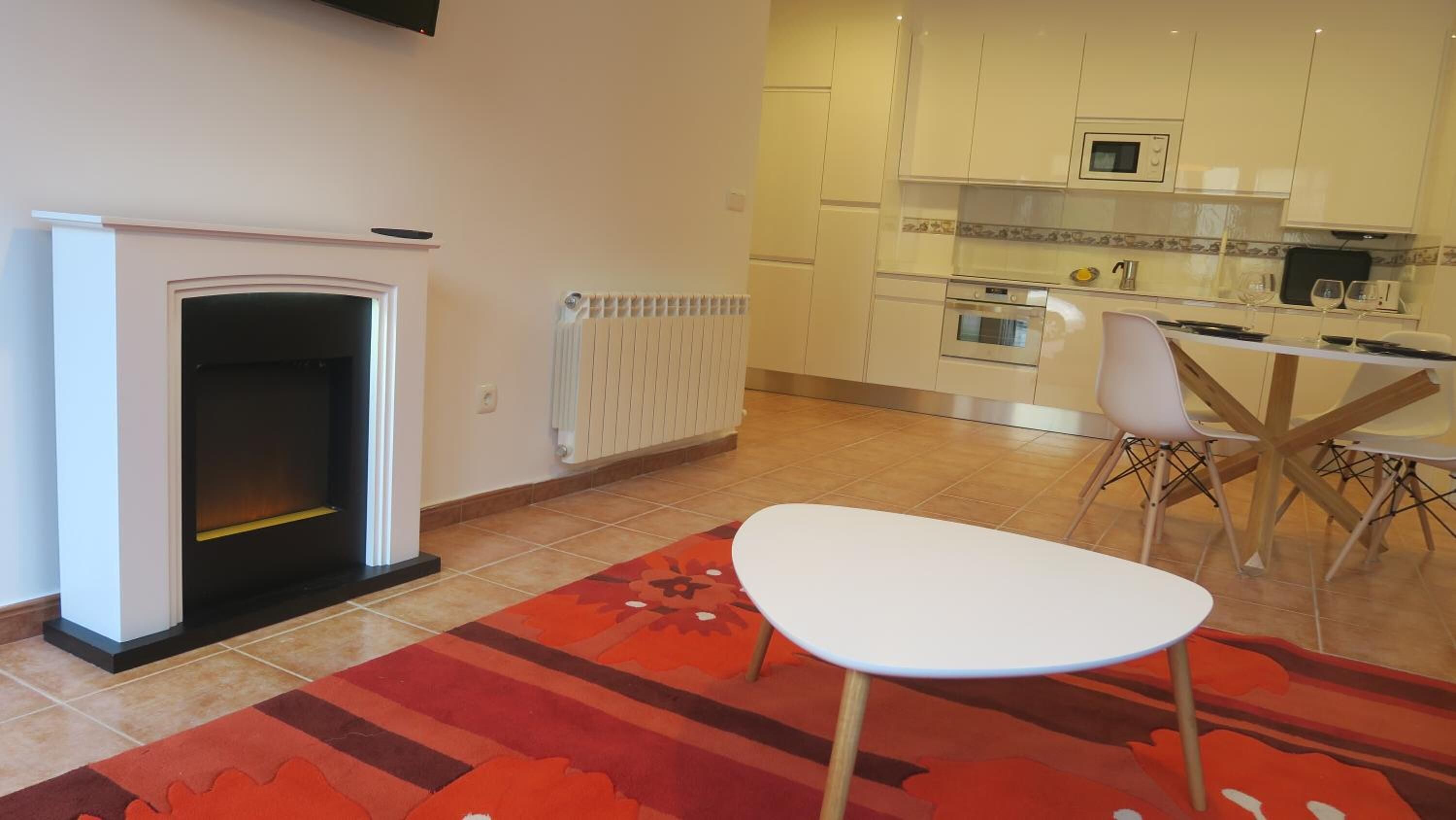 Un salon moderne avec une cheminée, un coin repas avec une table et des chaises, et une cuisine équipée d’appareils électroménagers.