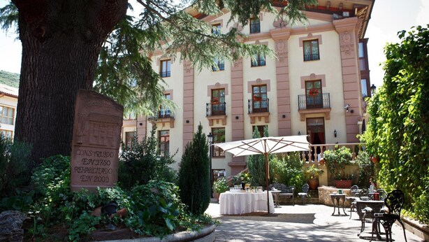 Un patio con un árbol grande, una mesa con mantel blanco y asientos exteriores.