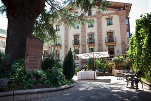 A courtyard with a large tree, a table with a white tablecloth, and outdoor seating. - Hotel Palacio Azcárate (Ezcaray)