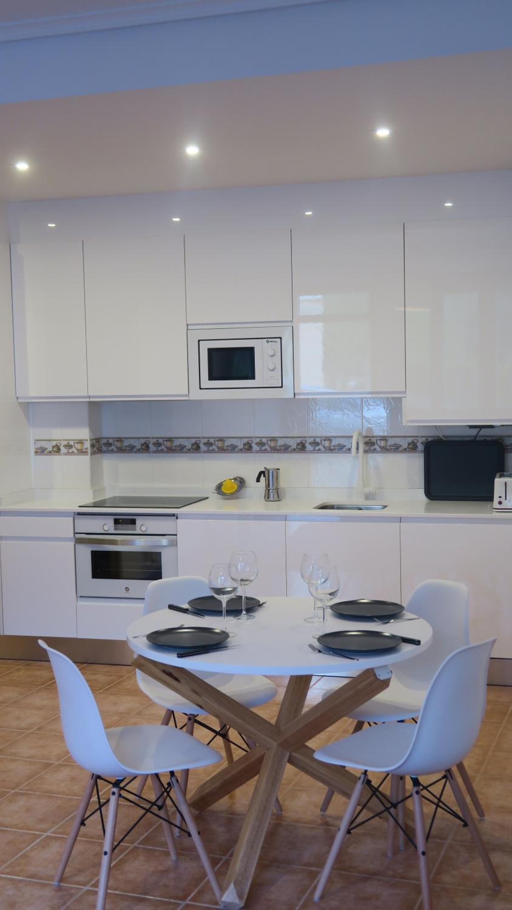 A modern kitchen with white cabinets, a microwave, a stove, and a dining area with a round table and four chairs.