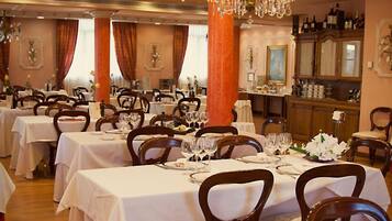 A formal dining room with multiple tables set for service, a large chandelier, and a bar area in the background.