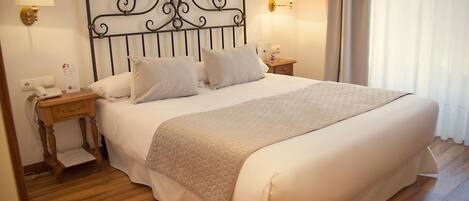A neatly made bed with a quilted blanket, two bedside tables with lamps, a telephone, and a wall-mounted light fixture.