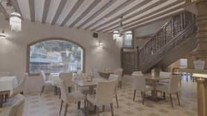 Un área de comedor con mesas y sillas redondas, un amplio ventanal con vistas y una escalera de madera.