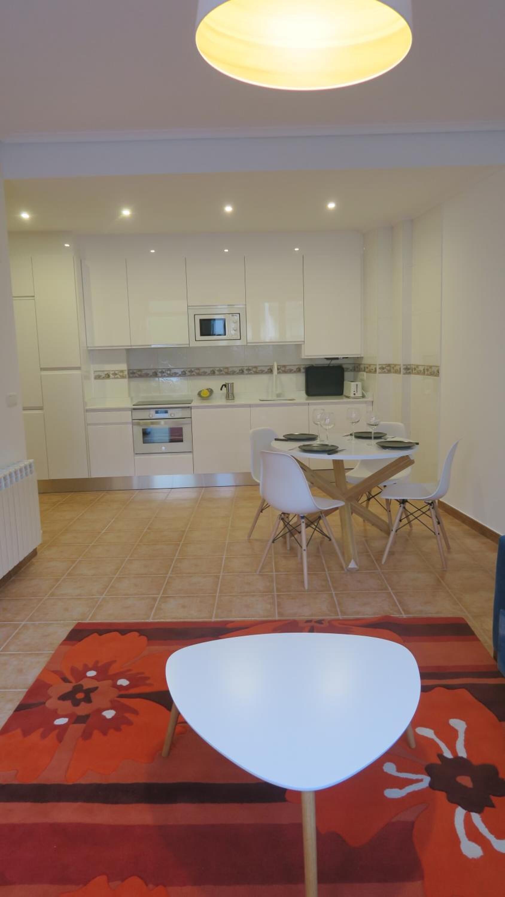 A modern kitchen with white cabinets, a microwave, and a dining area with a white table and chairs.