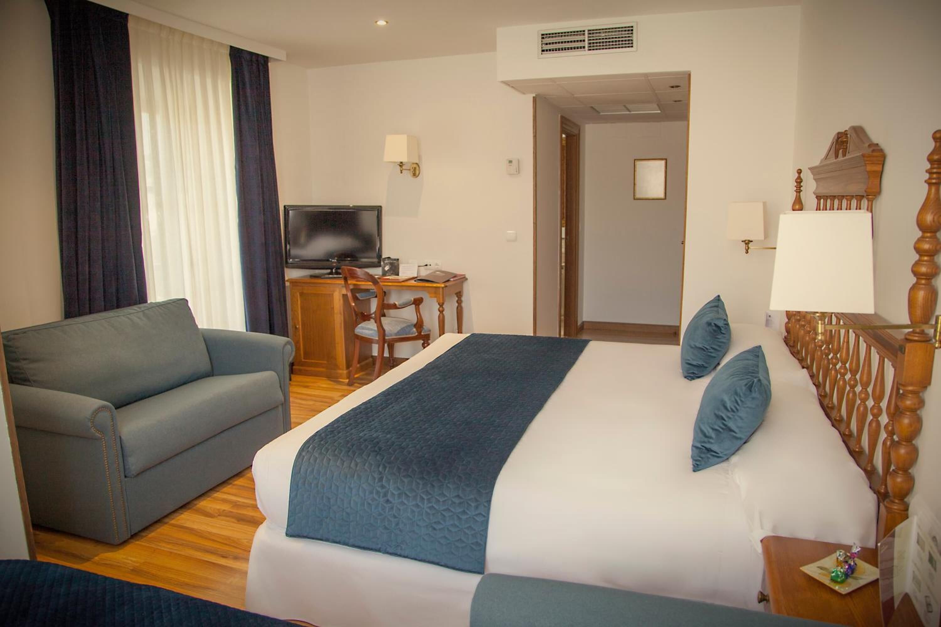 A hotel room with a bed, a sofa, a desk with a TV, and a lamp.