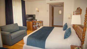 A hotel room with a bed, a sofa, a desk with a TV, and a lamp.