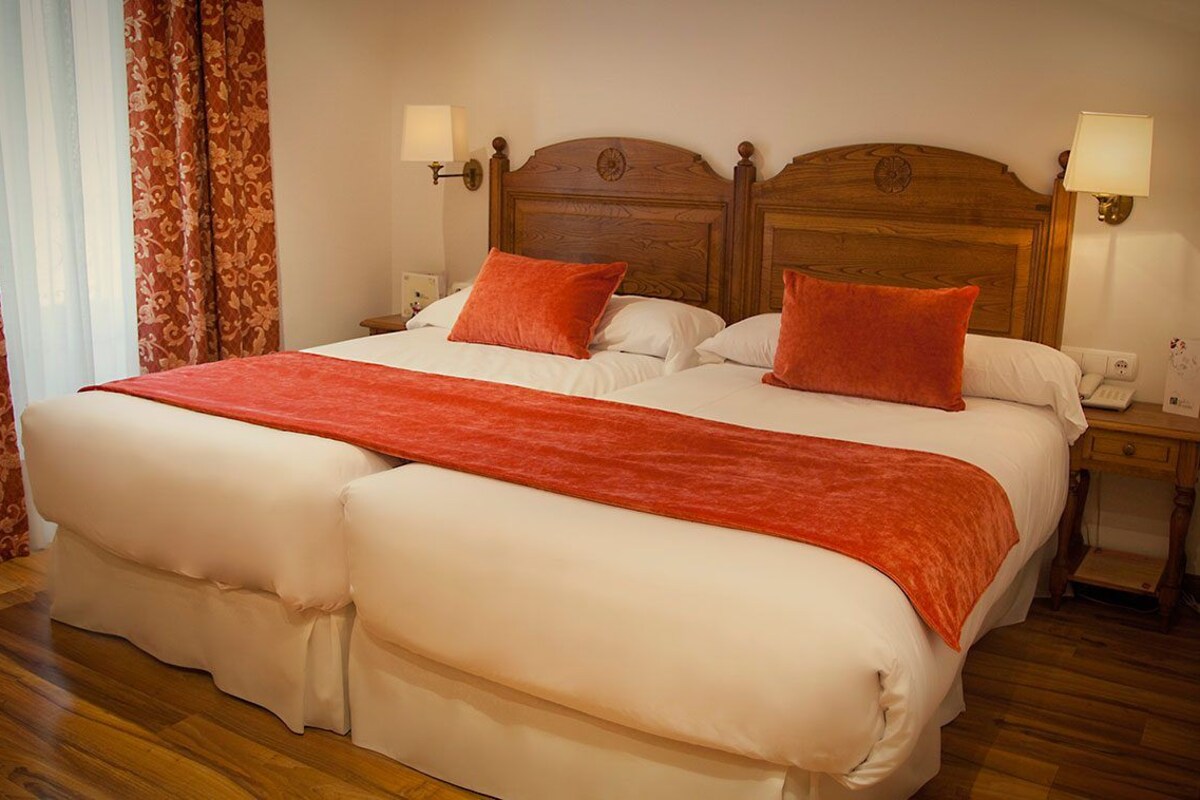 Una cama doble con cabecera de madera, dos mesitas de noche con lámparas y una colcha roja.