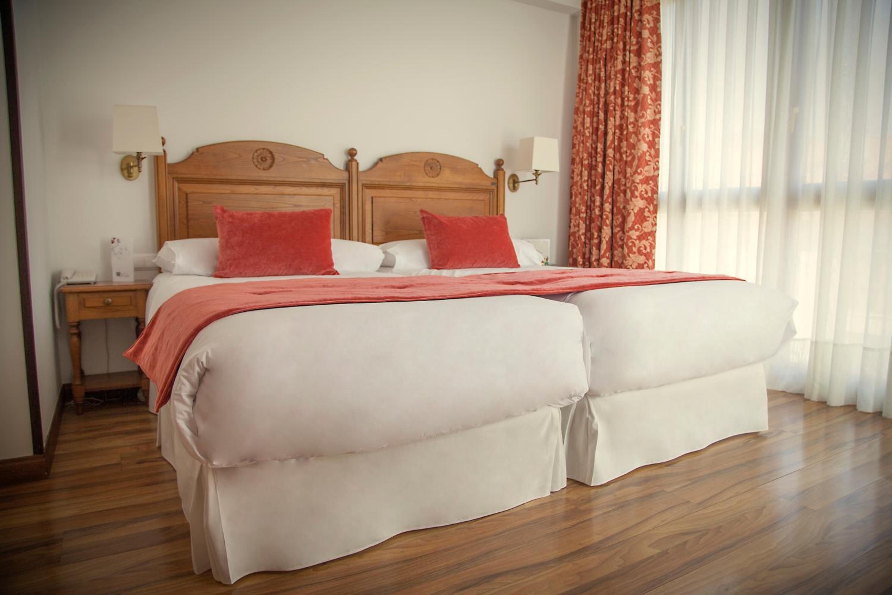 Una cama doble con cabecera de madera, dos mesitas de noche con lámparas y una ventana con cortinas.