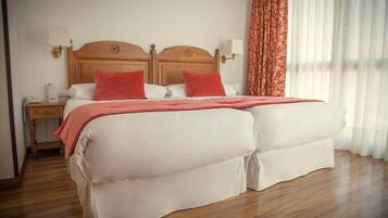 Una cama doble con cabecera de madera, dos mesitas de noche con lámparas y una ventana con cortinas.