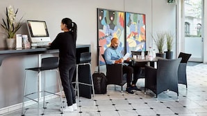 Zona de recepción de un hotel con computadora, asientos y una obra de arte en la pared.