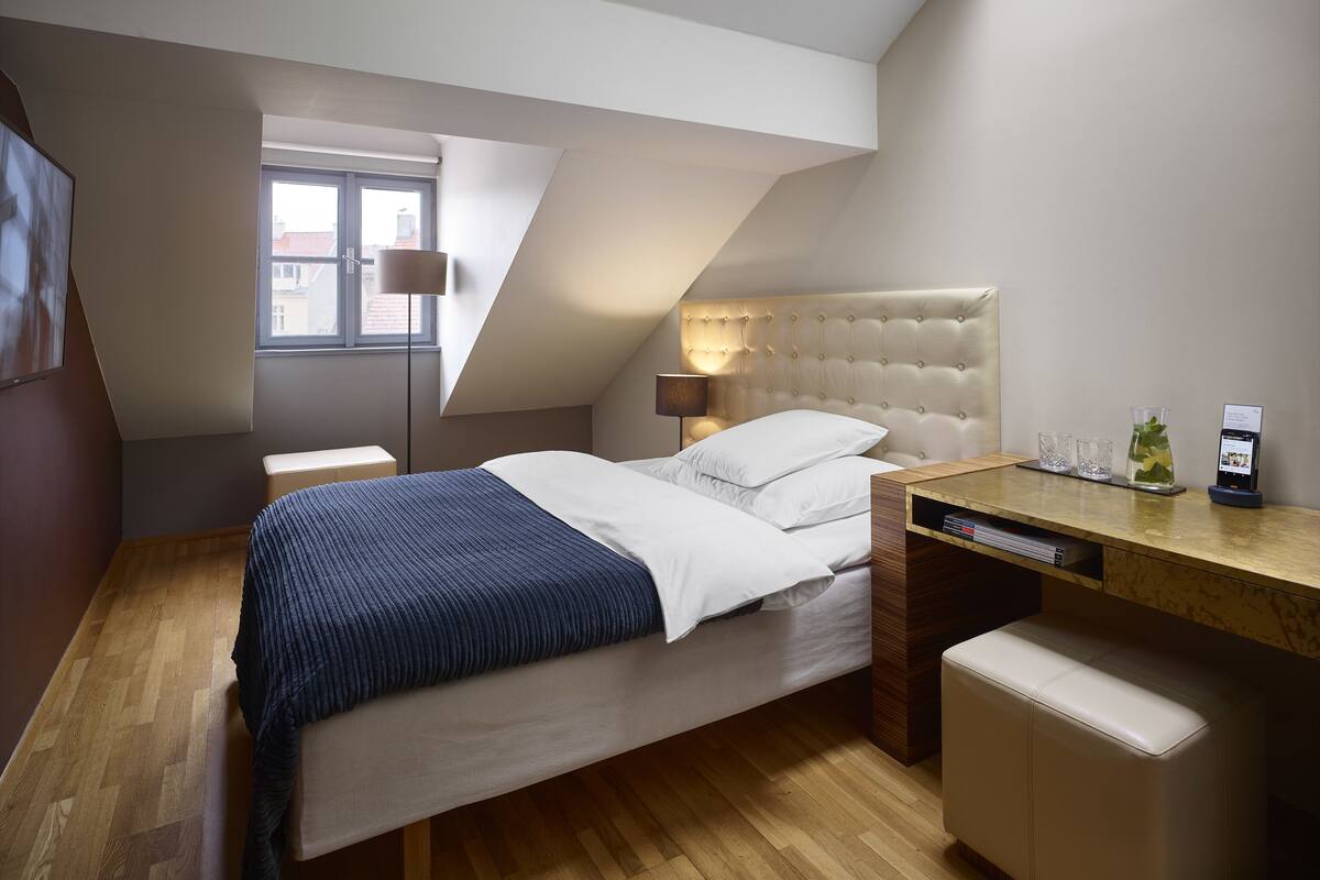 A bedroom with a bed, a desk, a chair, a lamp, and a window.