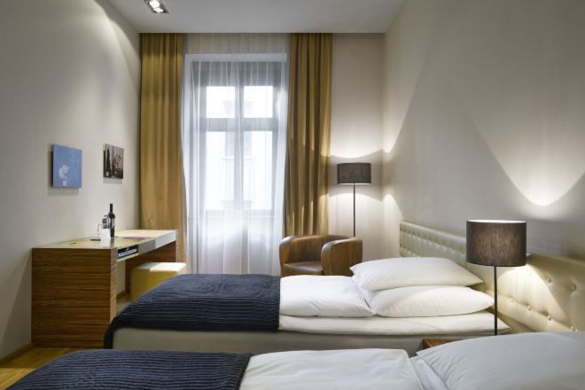 A hotel room with two beds, a desk, a chair, a lamp, and a window with curtains.