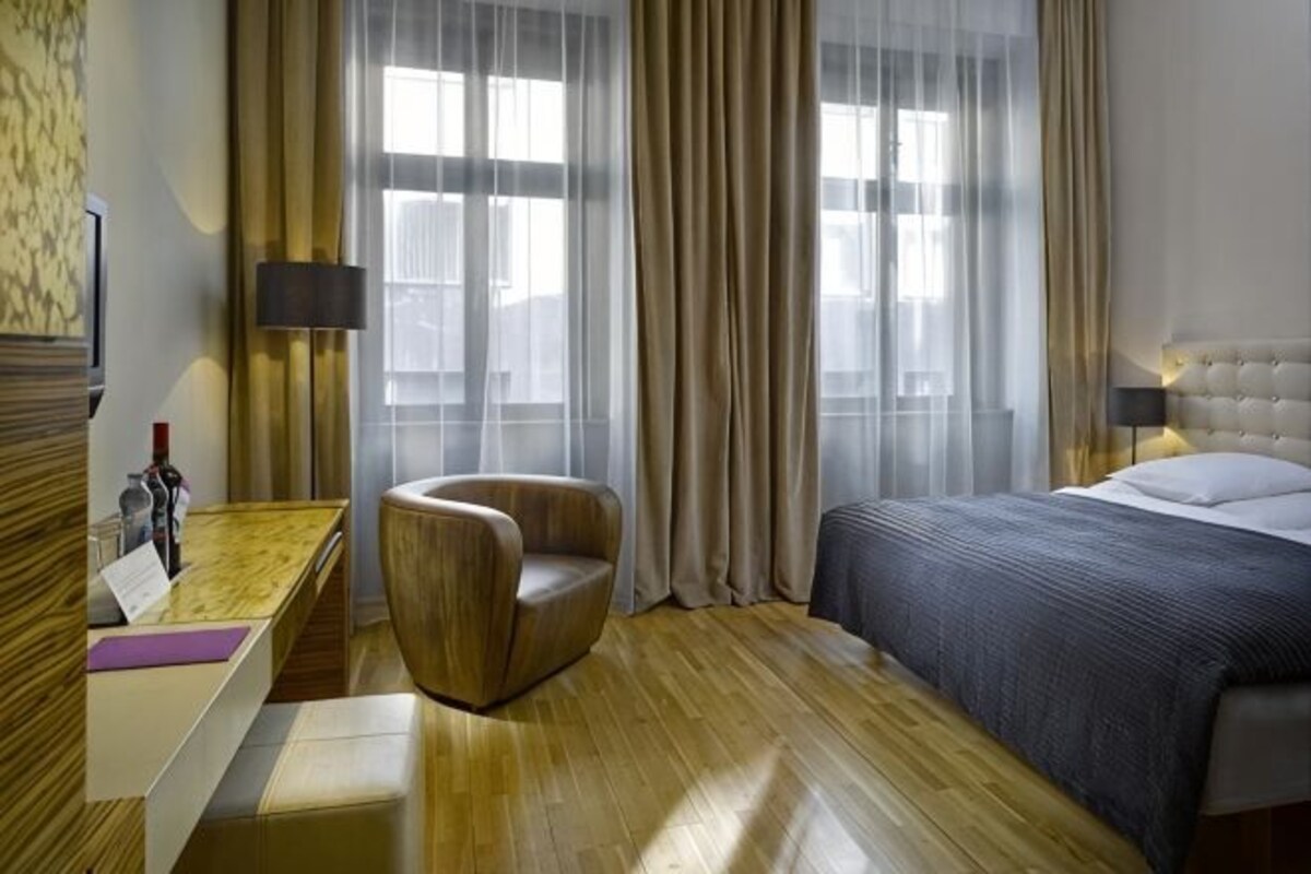 Una habitación de hotel con cama, una silla, escritorio y ventana con cortinas.